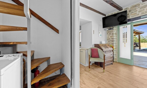 A staircase with wooden steps and a white wall, a wooden cabinet with drawers, a chair with a red cushion, and a television mounted on the wall. - Casa Chiara, Your Holiday Home with pool in Motovun, Istria (Motovun)