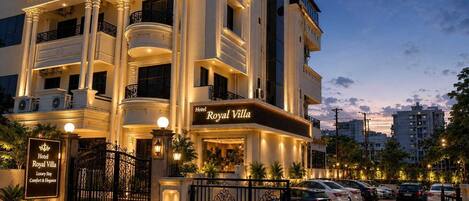 A multi-story hotel with a grand entrance, balconies, and a parking area.
