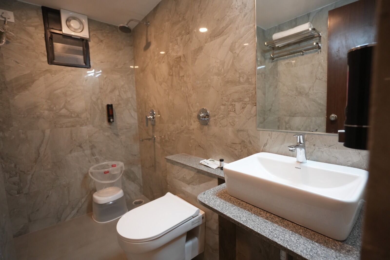A bathroom with a marble wall, a white sink, a toilet, and a shower.