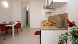 Eine moderne Küche mit Essbereich, einer Holztresenplatte, Obst, einer gewebten Vase und einem roten Stuhl.