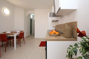 Eine moderne Küche mit Essbereich, einer Holztresenplatte, Obst, einer gewebten Vase und einem roten Stuhl.