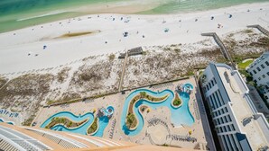 An aerial view of a beach resort with a large sandy beach, a swimming pool area, and adjacent buildings. - Phoenix Gulf Towers 2103 3 Bedroom Condo (Orange Beach)