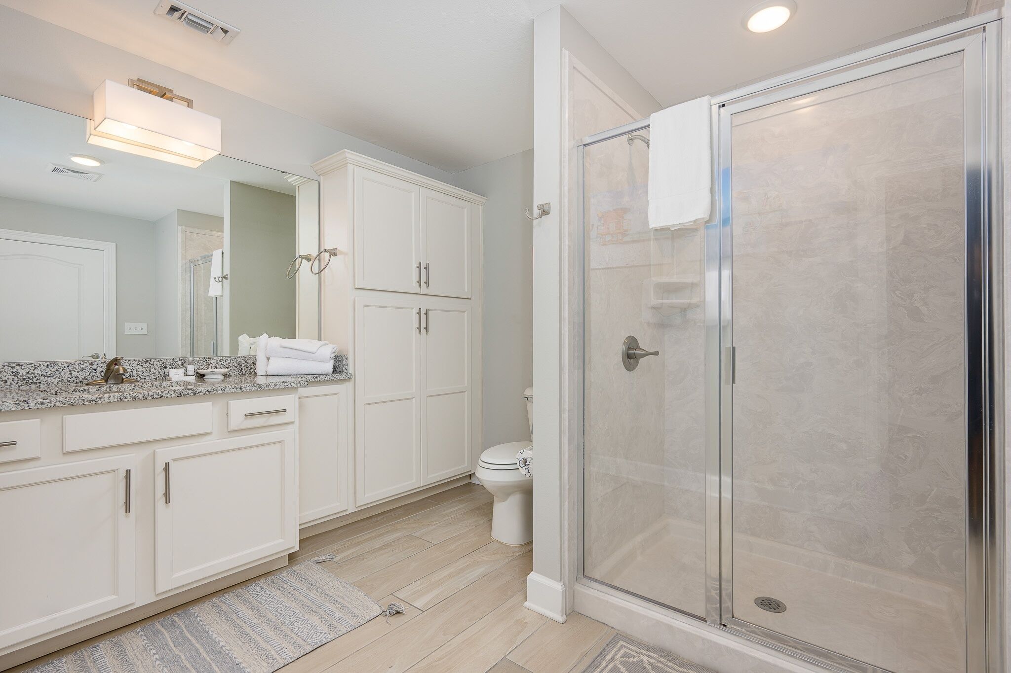 A modern bathroom with white cabinetry, a glass shower enclosure, and a granite countertop.