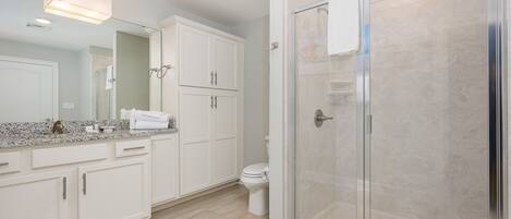 A modern bathroom with white cabinetry, a glass shower enclosure, and a granite countertop.