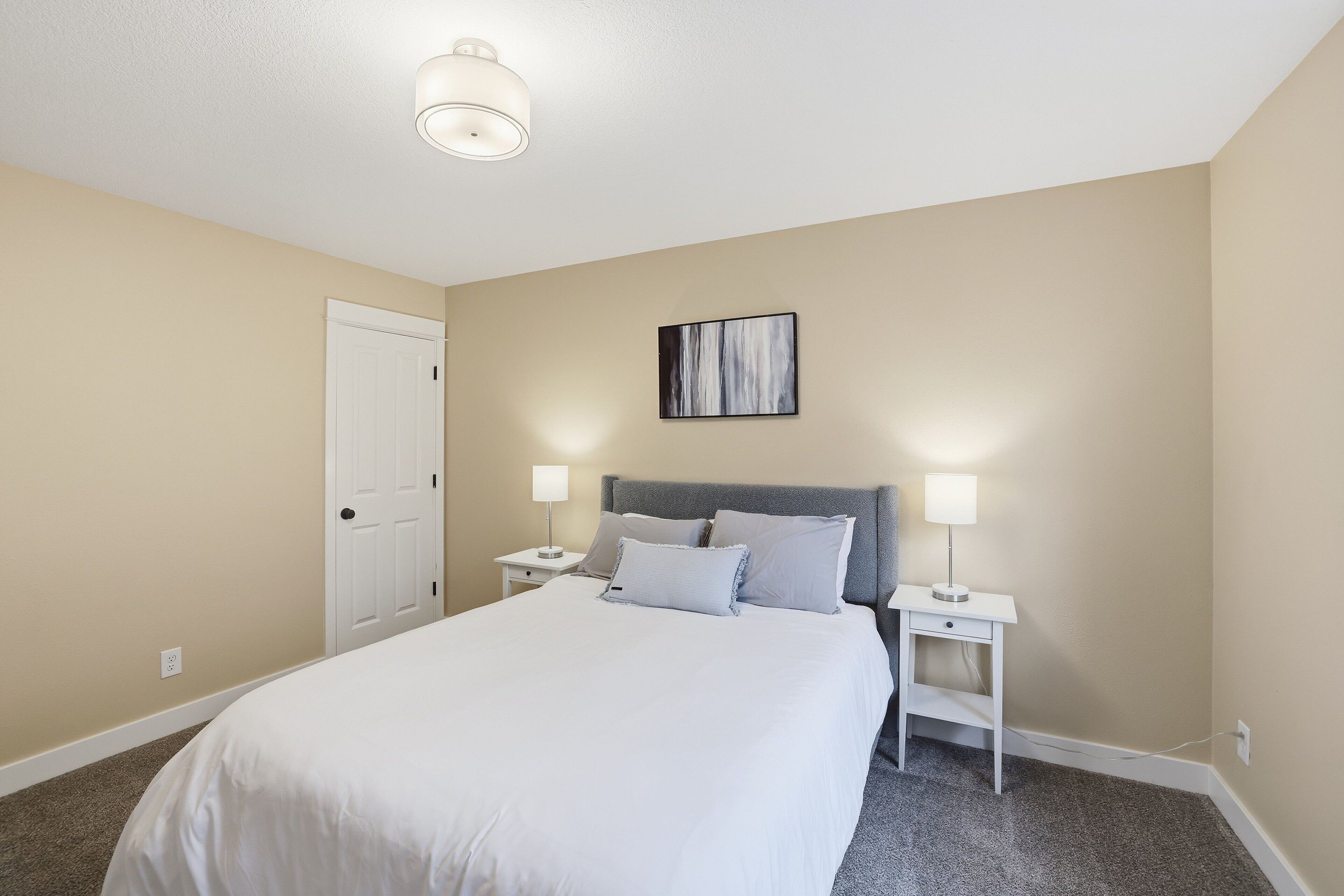 A bedroom with a bed, two bedside tables, a nightstand, a door, and a ceiling light fixture.