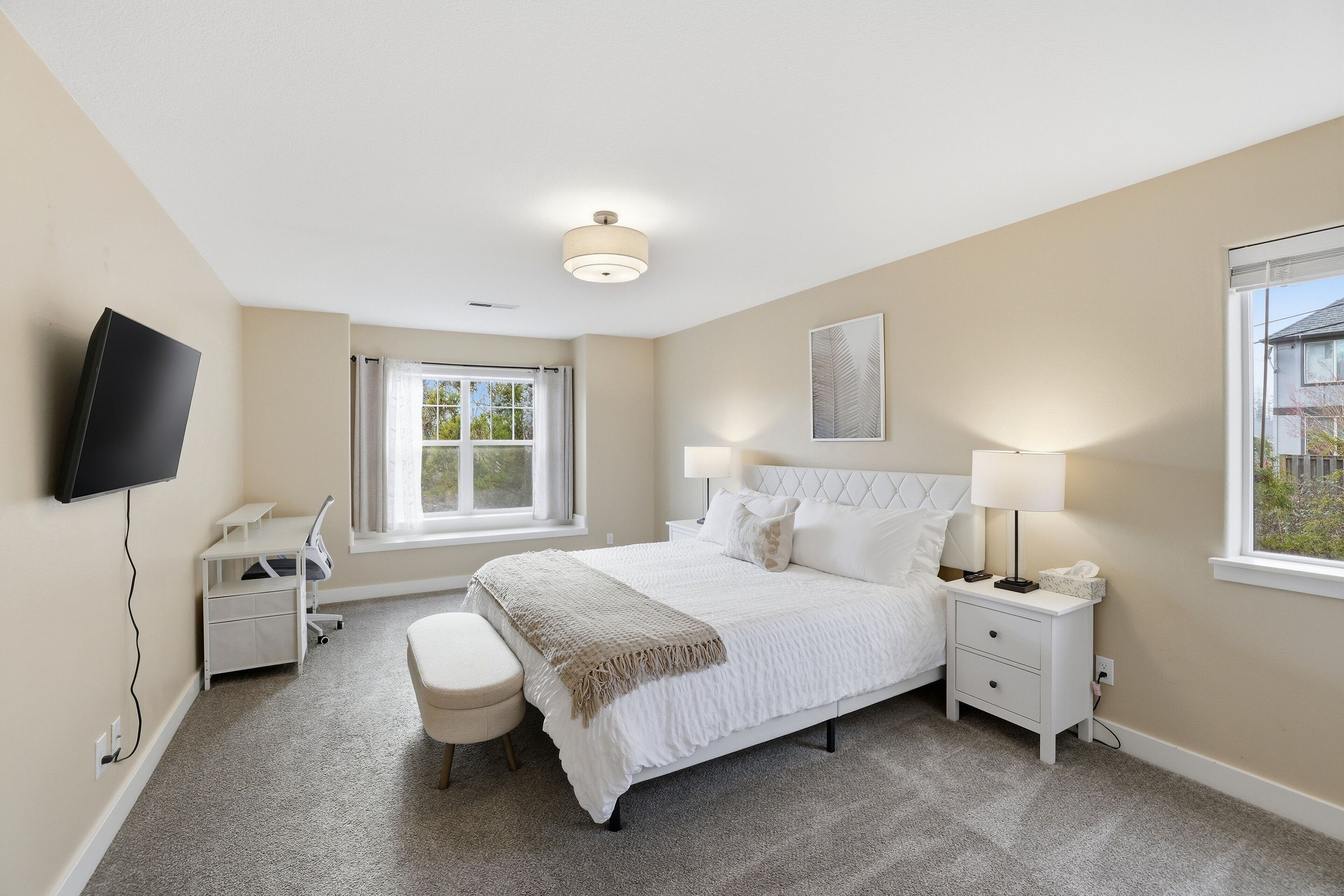 A bedroom with a bed, bedside tables, a desk, a chair, a TV mounted on the wall, and a window.