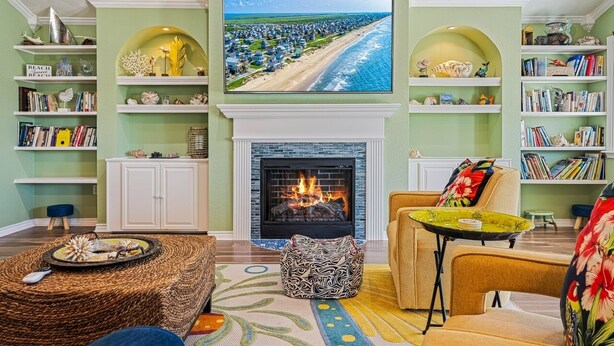 A living room with a fireplace, bookshelves, a television, and a view of a beach. - Casa Bella 4 Bedroom Home (Port Bolivar)