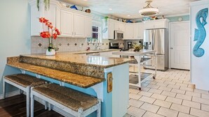 A kitchen with white cabinets, a granite countertop, and a central island with bench seating. - Casa Bella 4 Bedroom Home (Port Bolivar)