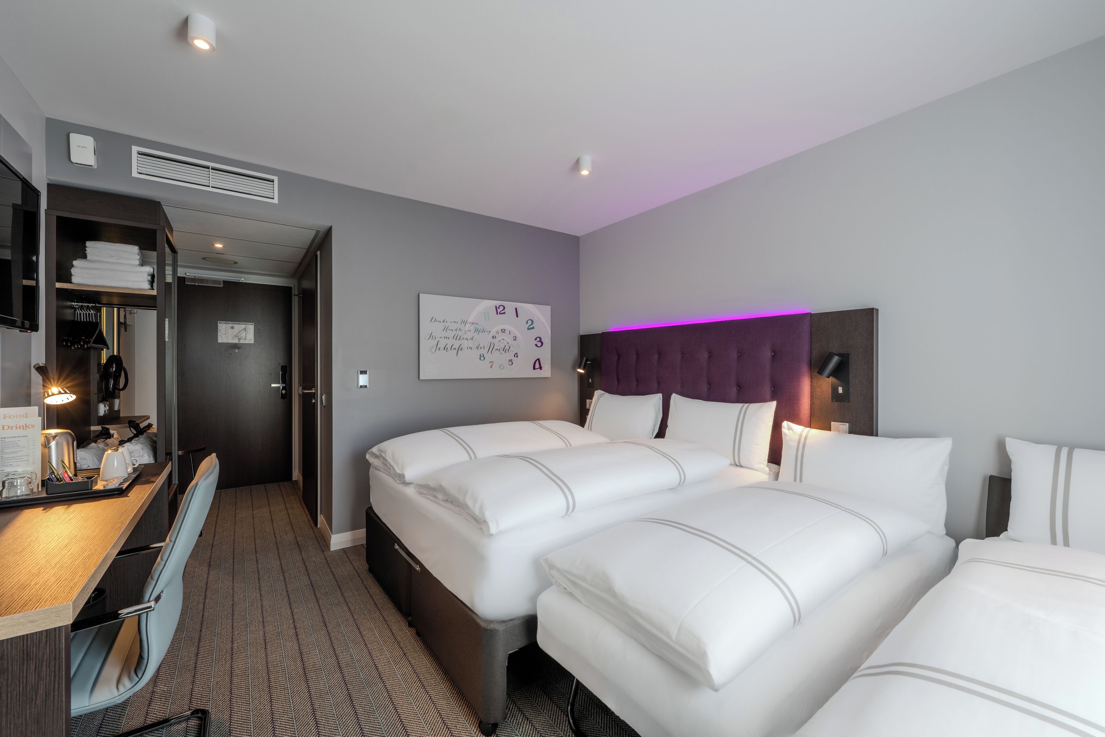 Une chambre d’hôtel avec deux lits, un bureau avec une chaise, une armoire et une horloge murale.