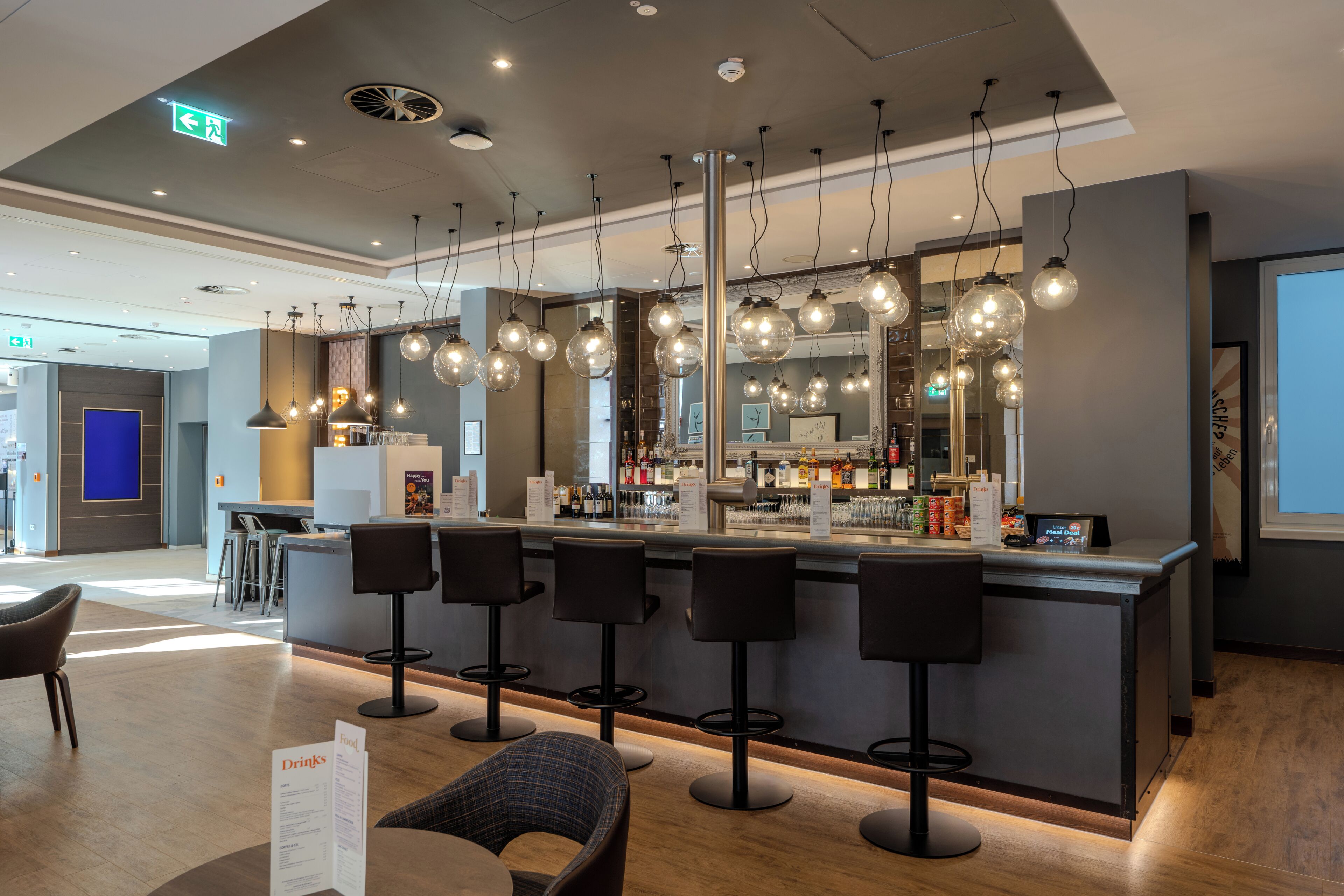 Een moderne bar met meerdere krukken, een toonbank met een menukaart en hangende lampen.