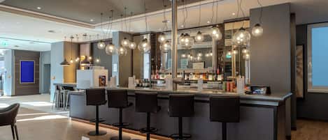 Un bar moderno con varios taburetes, una barra con menú y lámparas colgantes.