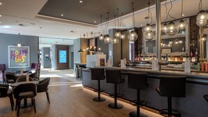 A modern bar area with a counter, bar stools, and hanging light fixtures. - Premier Inn Hannover City Centre (Hannover)