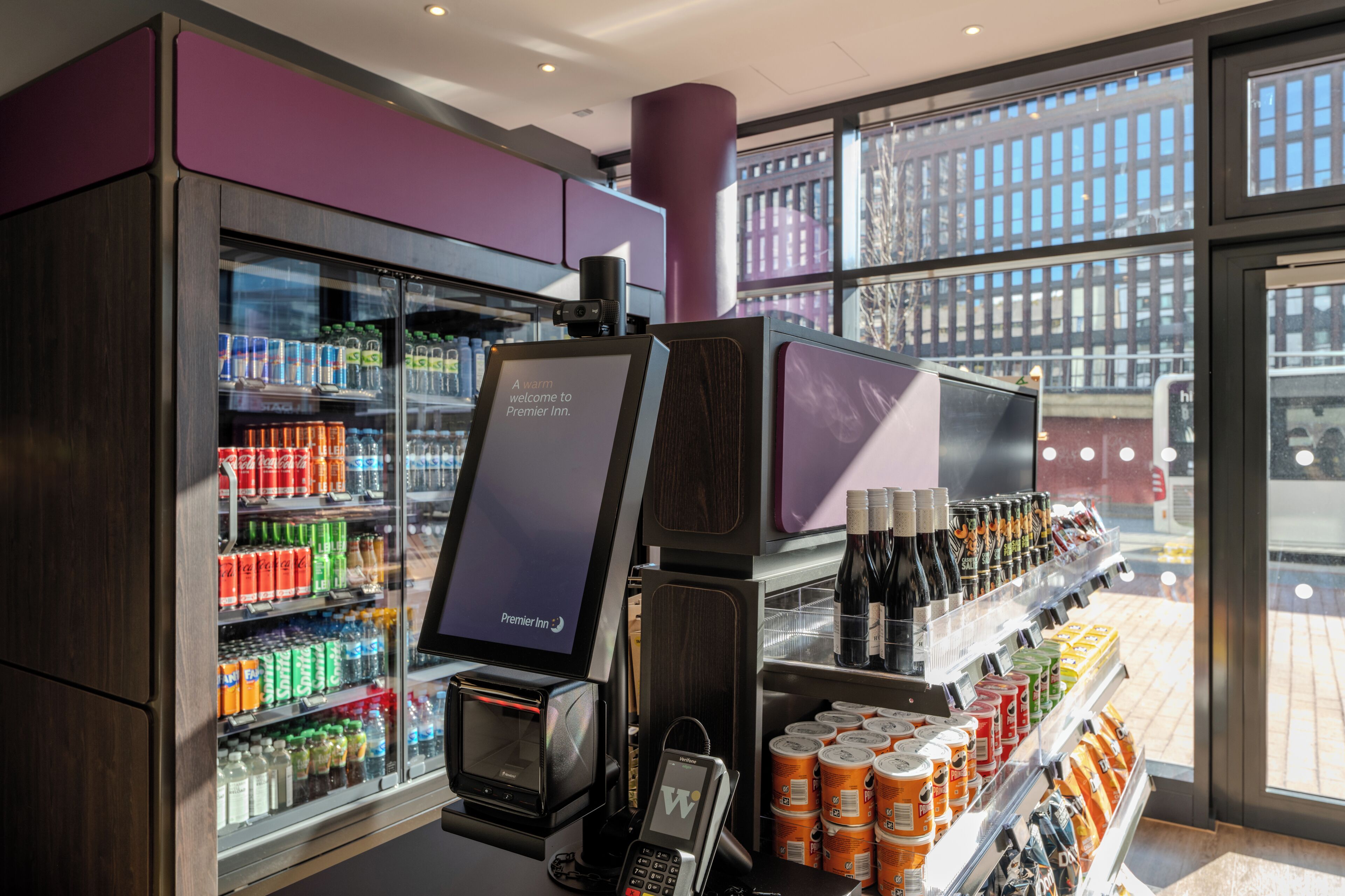 A self-service beverage kiosk with a variety of drinks and a digital screen displaying 'Premier Inn'.