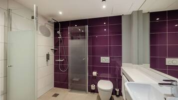 Un baño moderno con cabina de ducha de vidrio, inodoro blanco y lavabo grande.