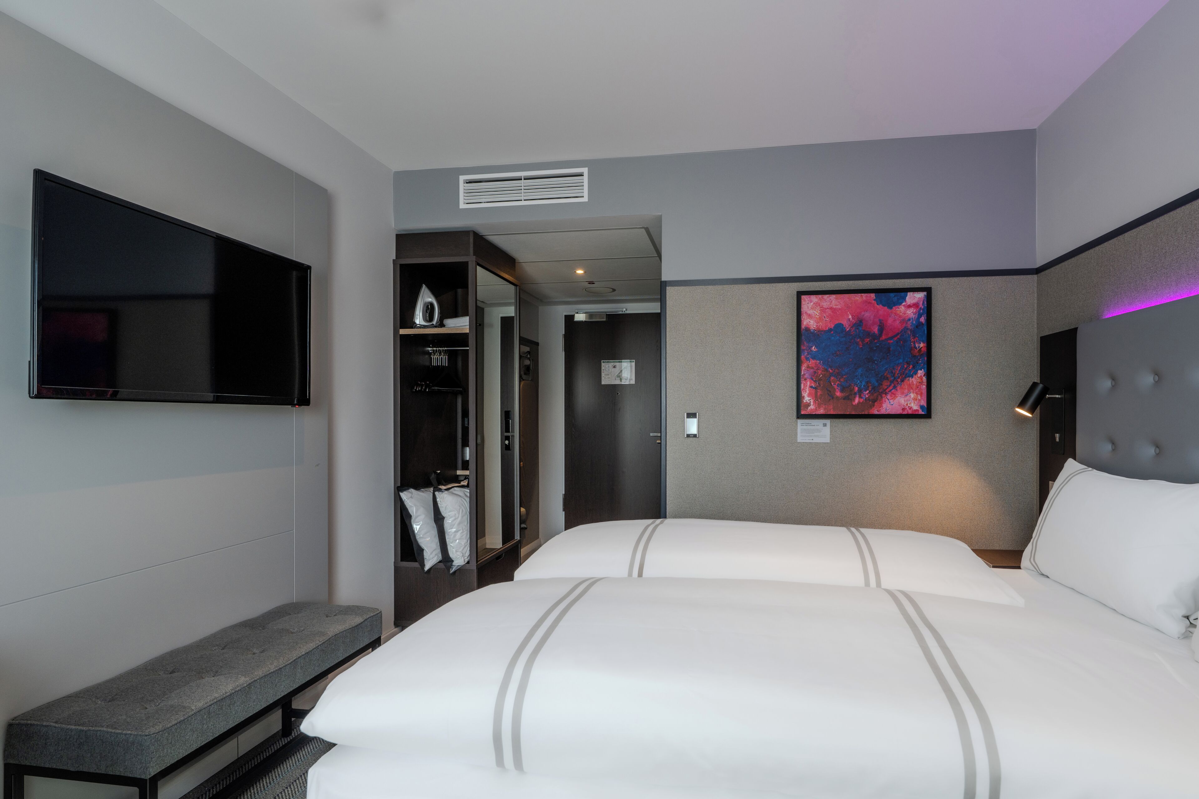 A hotel room with a large bed, a bench, a TV, a wardrobe, and a painting on the wall.