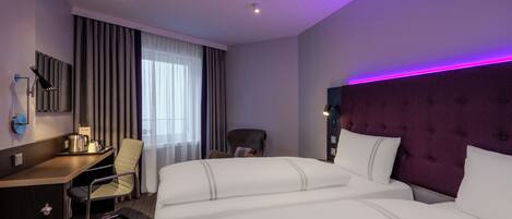 A hotel room with a bed, a desk, a chair, a headboard, and a window with curtains.