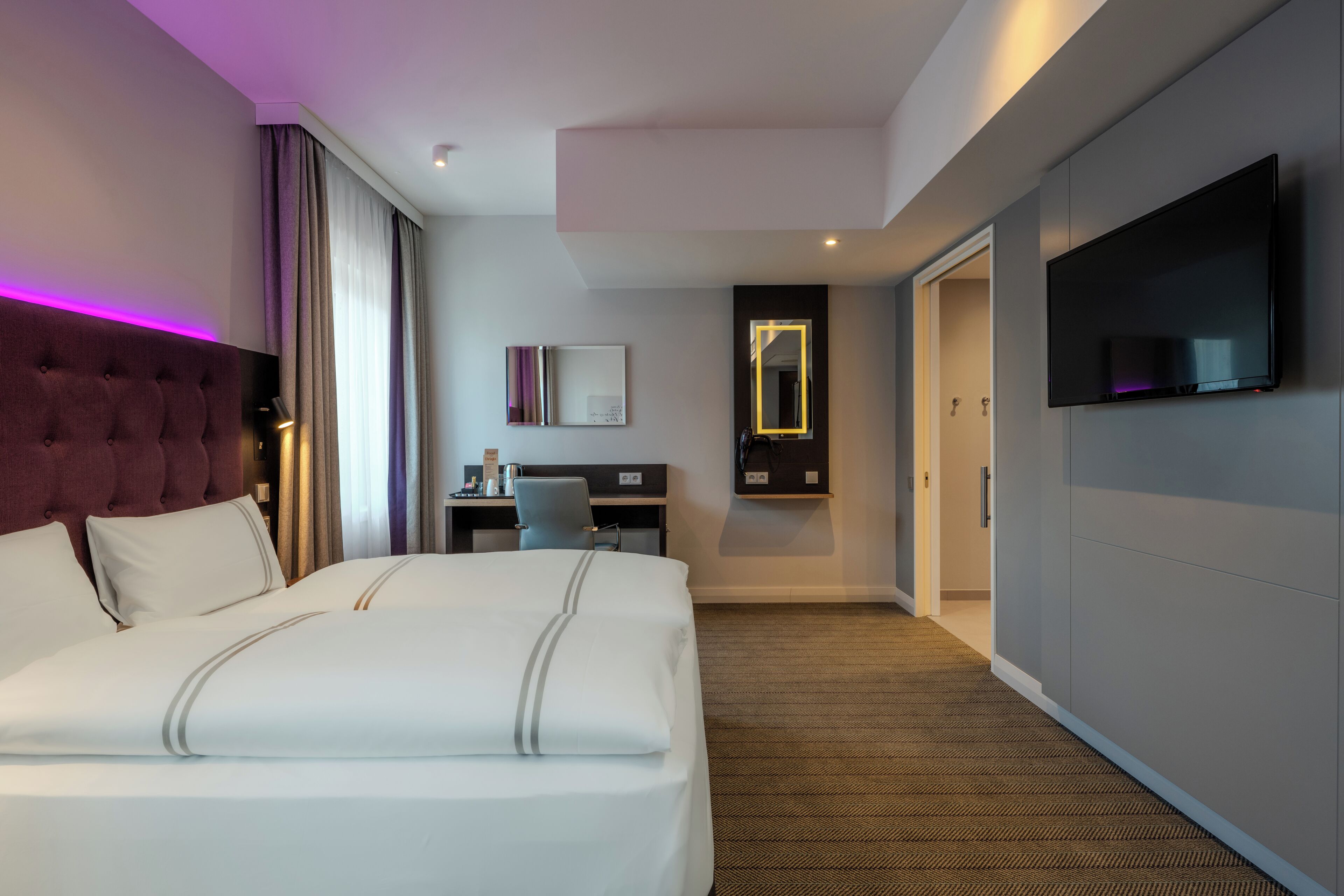 A hotel room with a large bed, a desk, a TV, and a mirror.
