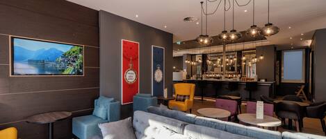 A modern lounge area with sofas, chairs, a bar, and a large TV screen.