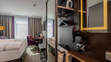 Une chambre d’hôtel avec deux lits, un bureau avec une chaise, un miroir, une armoire et une valise.