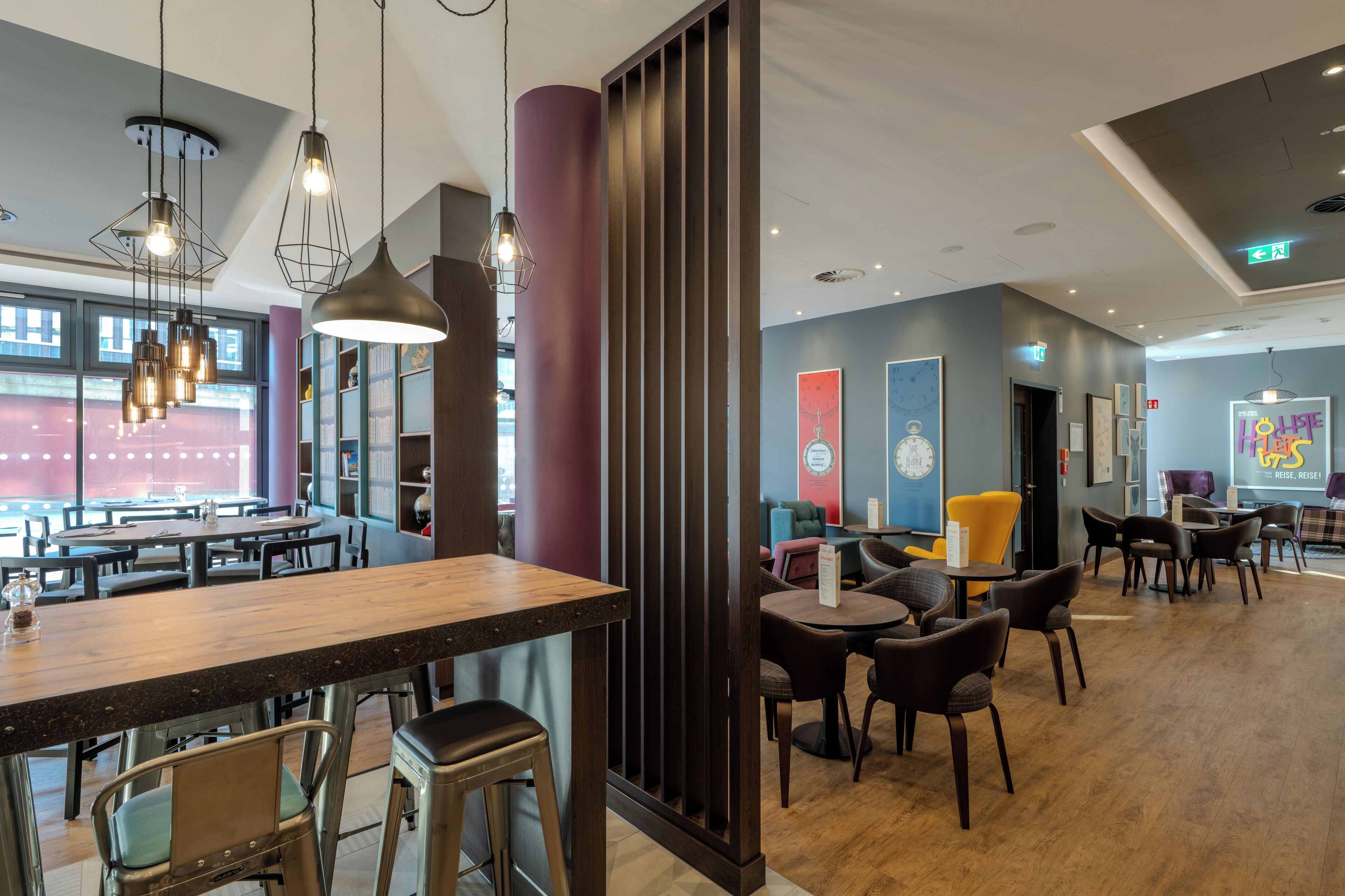 Un interior de restaurante moderno con mesas de madera, sillas de metal, iluminación colgante y un gran ventanal.