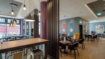 Ein modernes Restaurant mit Holztischen, Metallstühlen, Pendelleuchten und einem großen Fenster.