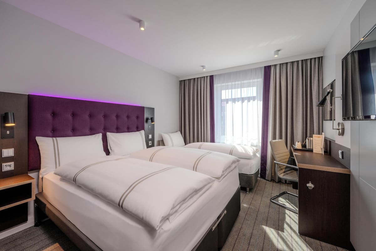 Une chambre d’hôtel avec deux lits, un bureau, une chaise, une télévision et une fenêtre avec des rideaux.