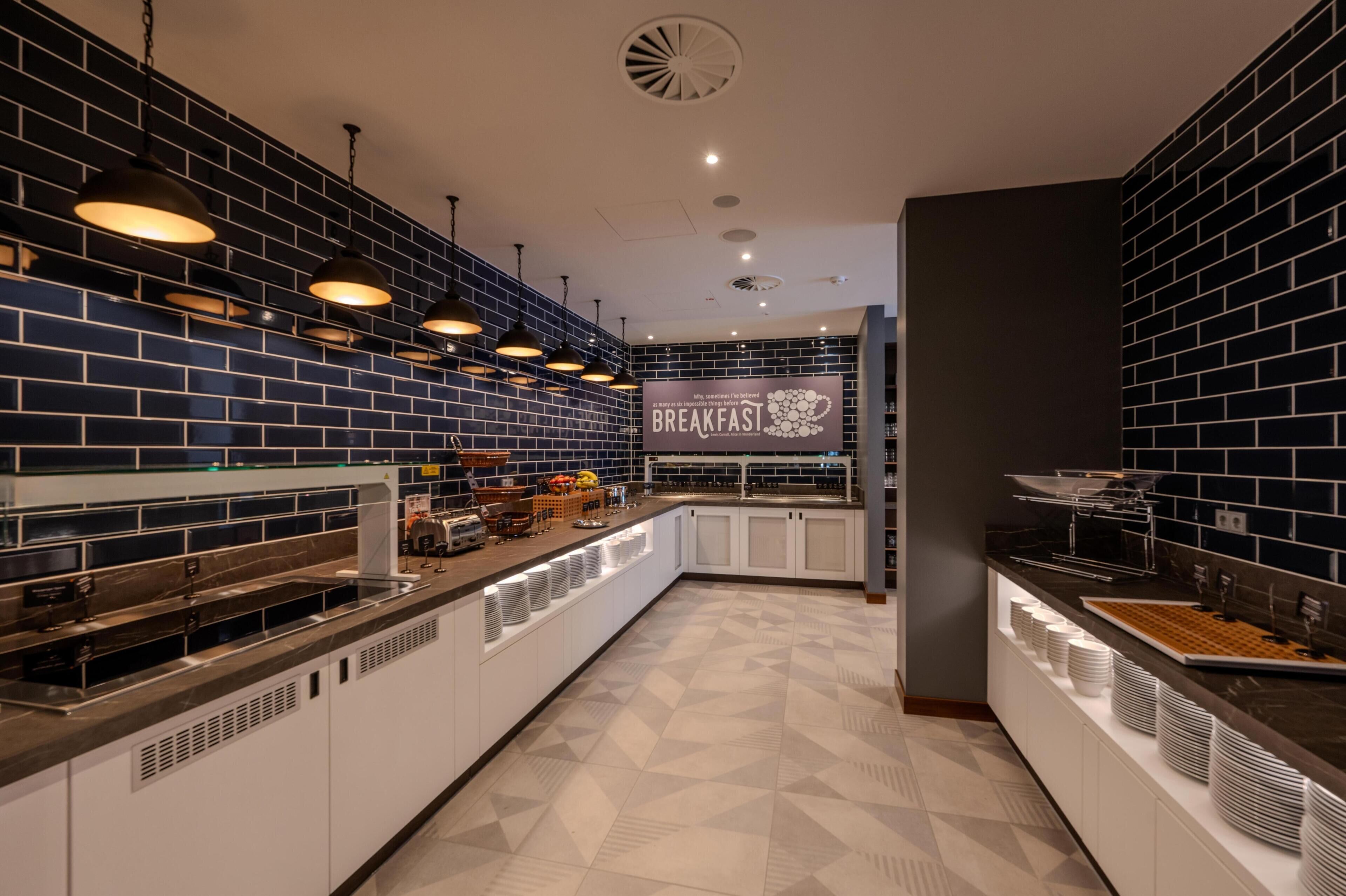 Un área de desayuno moderna con un letrero que dice 'BREAKFASTSI', que presenta una pared de ladrillo, iluminación colgante y una disposición tipo bufé.