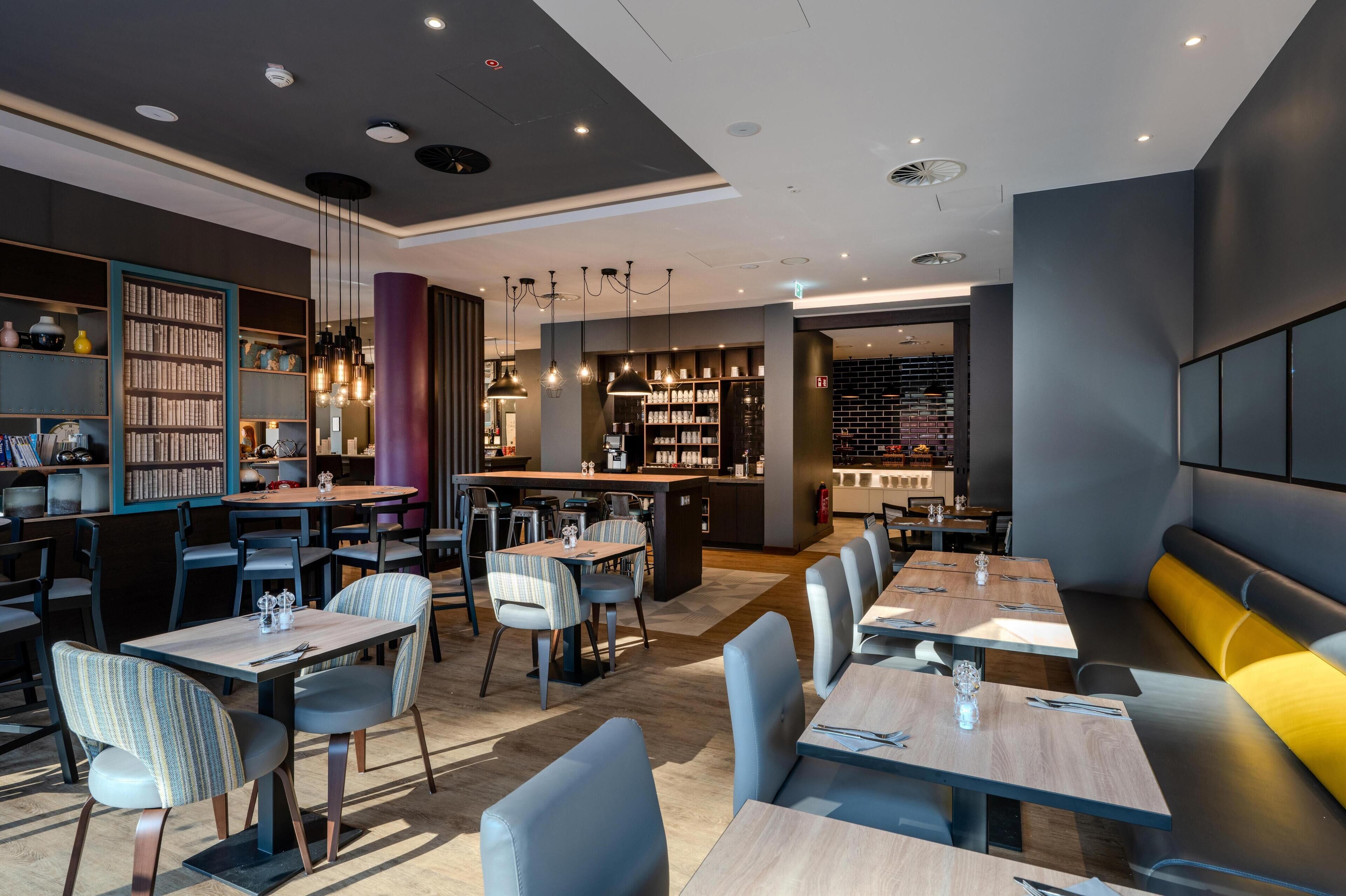 A modern restaurant with multiple seating areas, including tables and booths, and a visible bar area.
