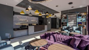A modern hotel lobby with a reception desk, seating area, and a large bookshelf. - Premier Inn Hannover City Centre (Hannover)