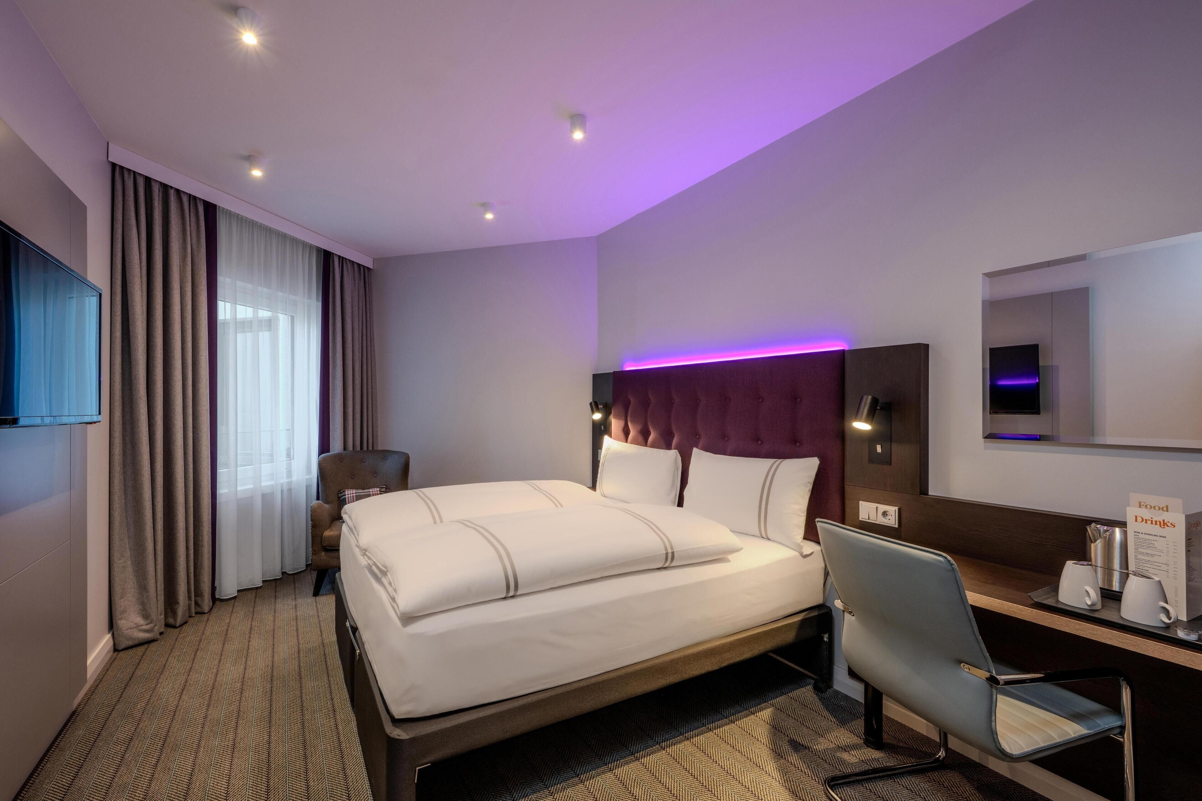 A hotel room with a bed, a desk, a chair, a television, and a sign indicating food and drinks.