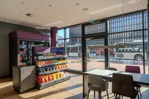 Un interior moderno con una máquina expendedora, estantes con snacks y vista a la calle.