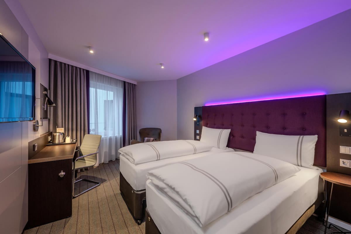 Une chambre d’hôtel avec deux lits, un bureau, une chaise, une télévision et un mur d’accent de couleur violette.