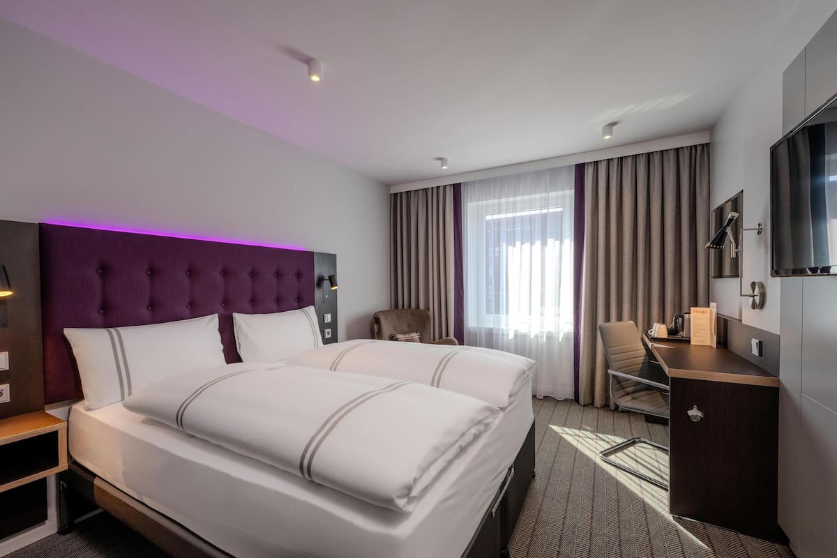 Une chambre d’hôtel avec un grand lit, un bureau, une chaise, une télévision et une fenêtre avec des rideaux.