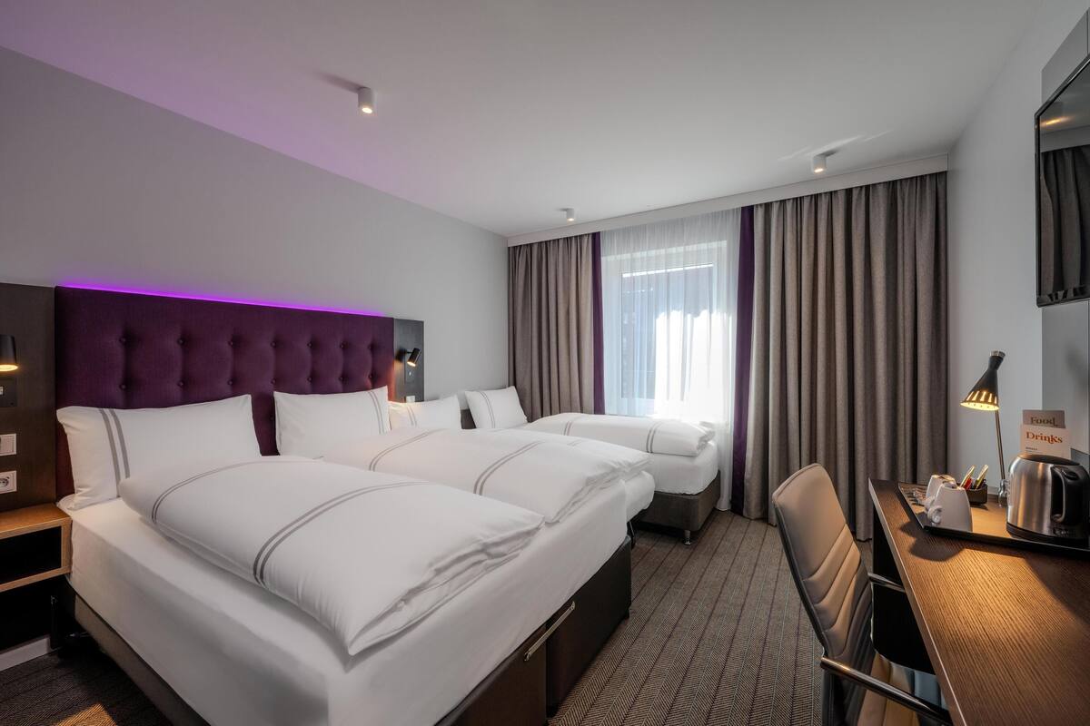 Une chambre d’hôtel avec deux lits, un bureau avec une lampe, une chaise, une télévision et un panneau indiquant où trouver de la nourriture et des boissons.