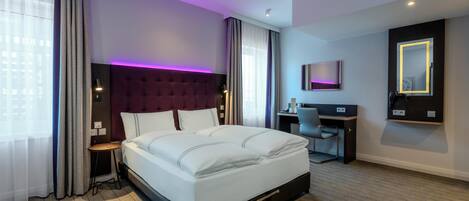 Habitación de hotel con una cama grande, un escritorio, una silla, un televisor y un espejo.