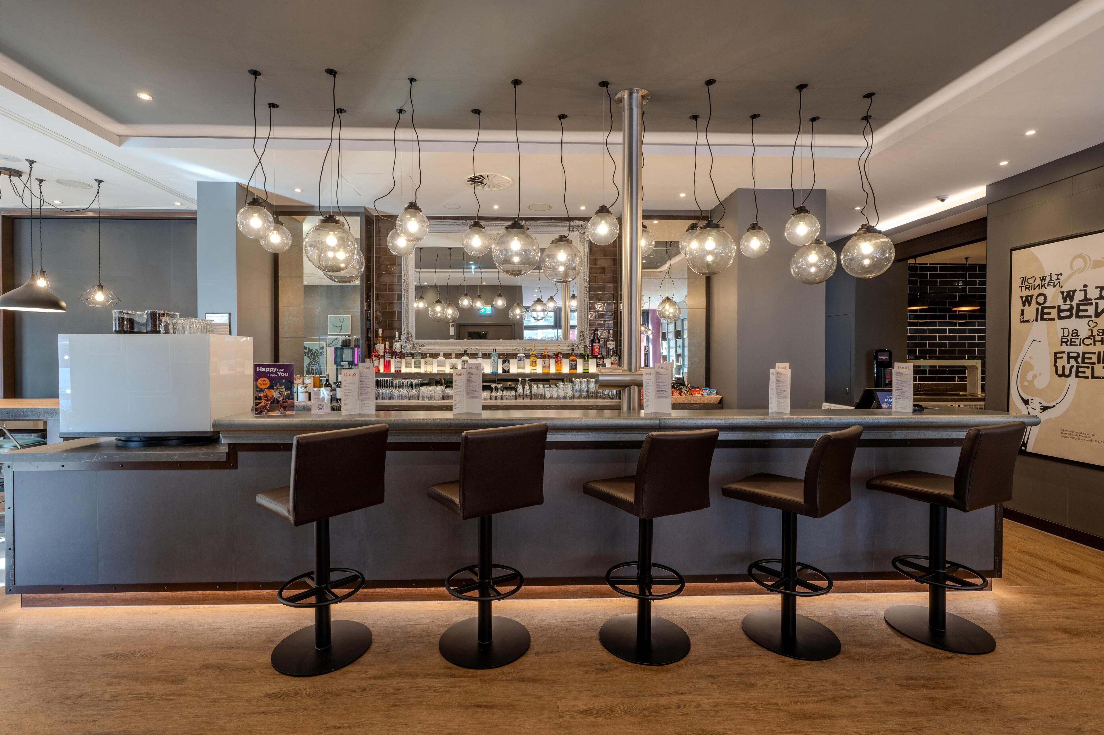 A bar area with a counter, multiple hanging light fixtures, and bar stools.