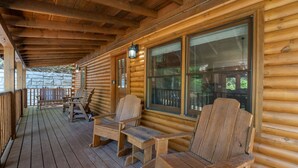 A wooden cabin with a porch, wooden chairs, and a stone wall in the background. - Er39 2 Bedroom Cabin (Pigeon Forge)