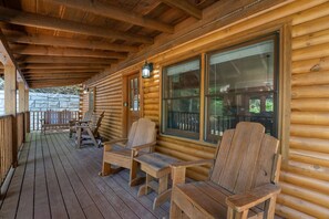 A wooden cabin with a porch, wooden chairs, and a stone wall in the background. - Er39 2 Bedroom Cabin (Pigeon Forge)