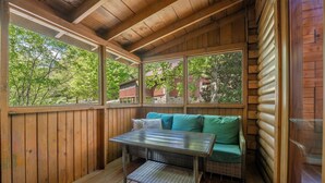 A wooden cabin interior with a table and green sofa, large windows, and wooden walls. - Er39 2 Bedroom Cabin (Pigeon Forge)