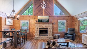 A log cabin interior with a stone fireplace, wooden dining table, and a large window. - Er39 2 Bedroom Cabin (Pigeon Forge)