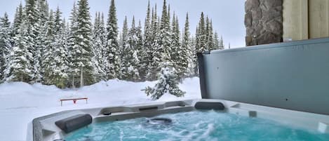A hot tub with a view of snow-covered trees and a stone wall.