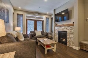 A living room with a fireplace, two sofas, a coffee table, and a TV mounted on the wall. - Echo Landing #26 2 Bedroom Home (Sun Peaks)