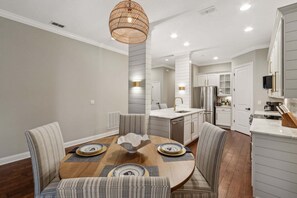 A modern kitchen with white cabinets, stainless steel appliances, and a dining area with striped chairs and a wooden table. - Summerwoods 1903 2 Bedroom Condo (Fernandina Beach)