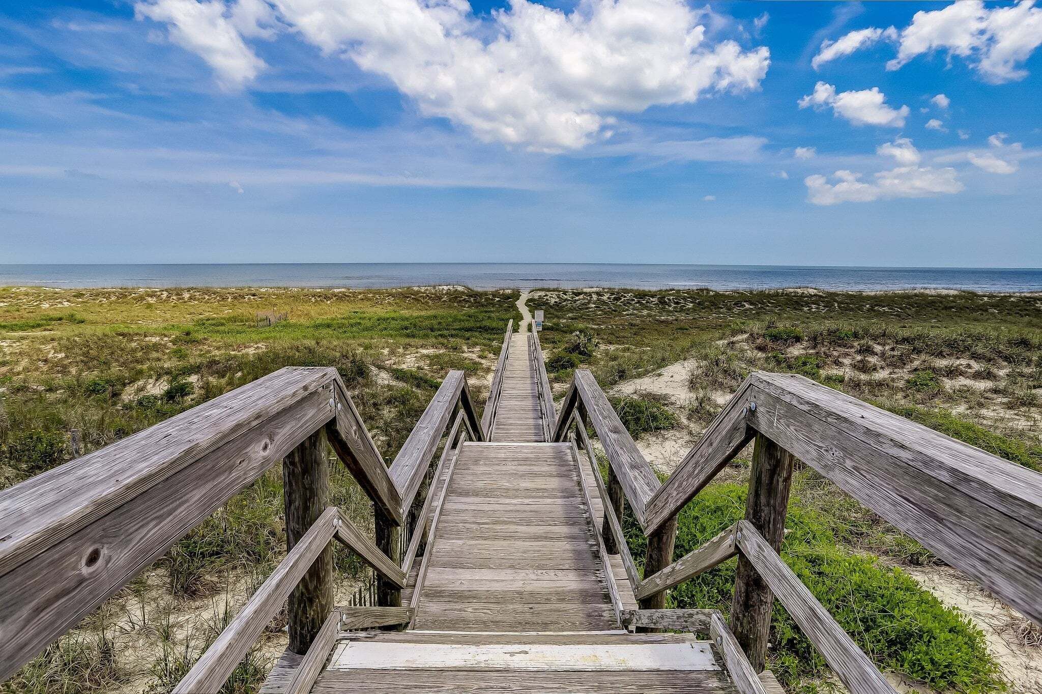 A wooden boardwalk leading to a beach with a clear sky.