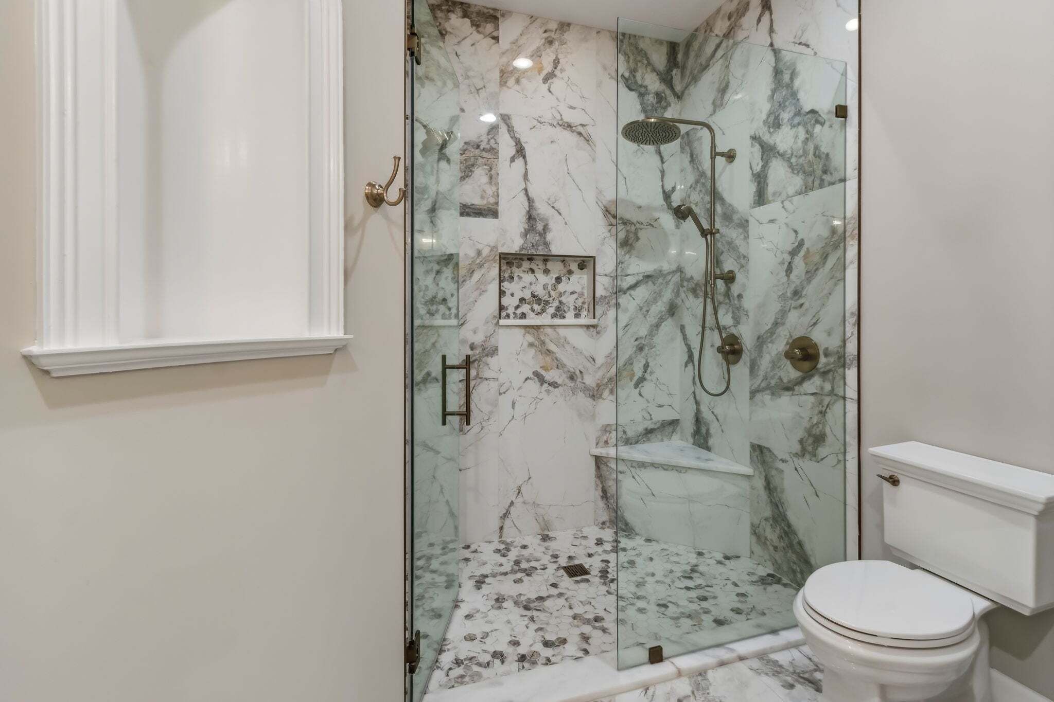 A bathroom with a glass-enclosed shower, marble walls, and a white toilet.