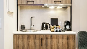 Et lille køkken med træskabe, en stålvask, elkedel og kaffemaskine.