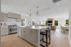 A modern kitchen with white cabinetry, a central island, and pendant lighting. - AMAZING NEW HOME, STEPS FROM LIGHTHOUSE BEACH! (Chatham)