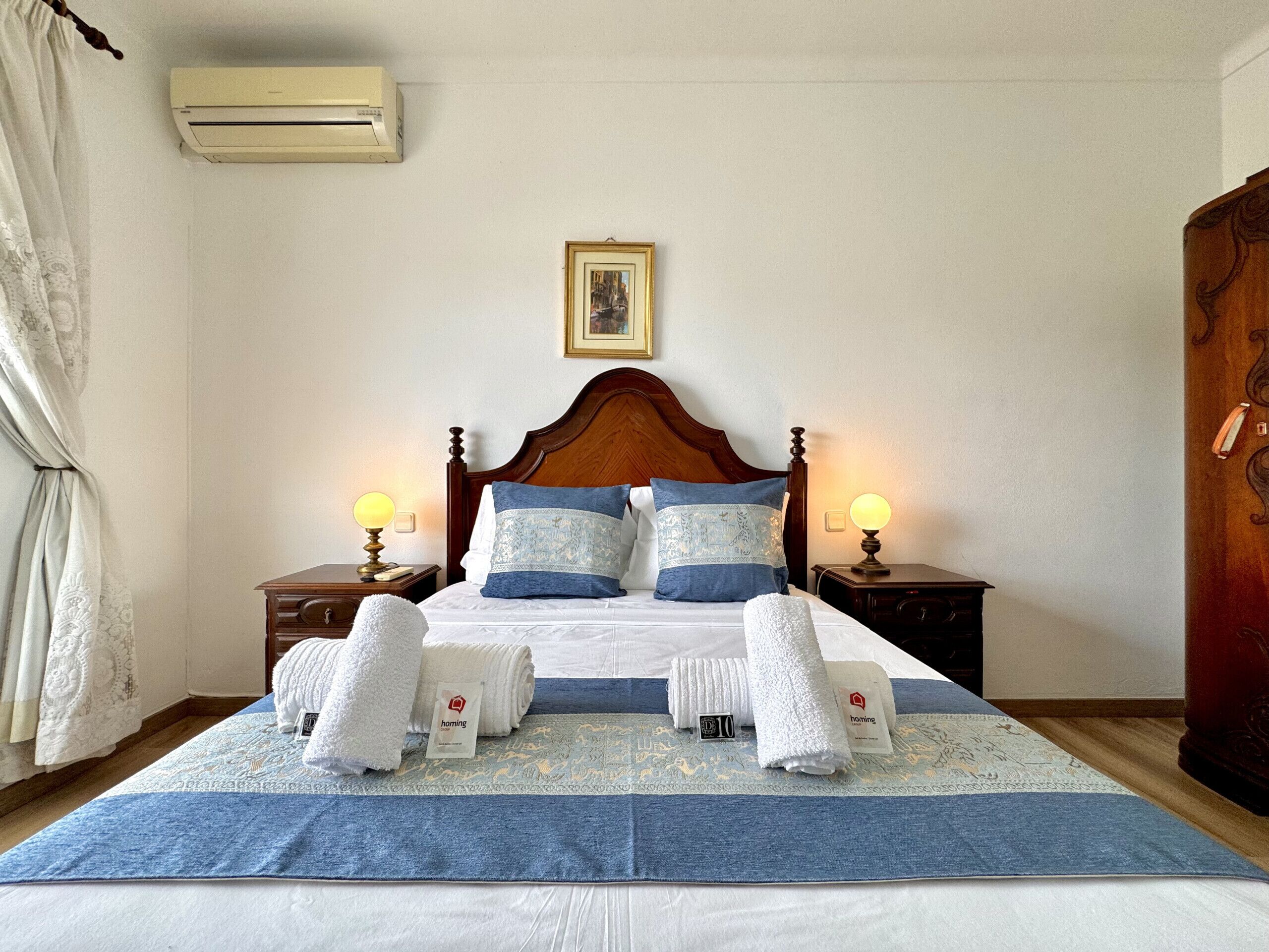 A neatly made bed with white linens, two bedside lamps, and a framed picture above the headboard.