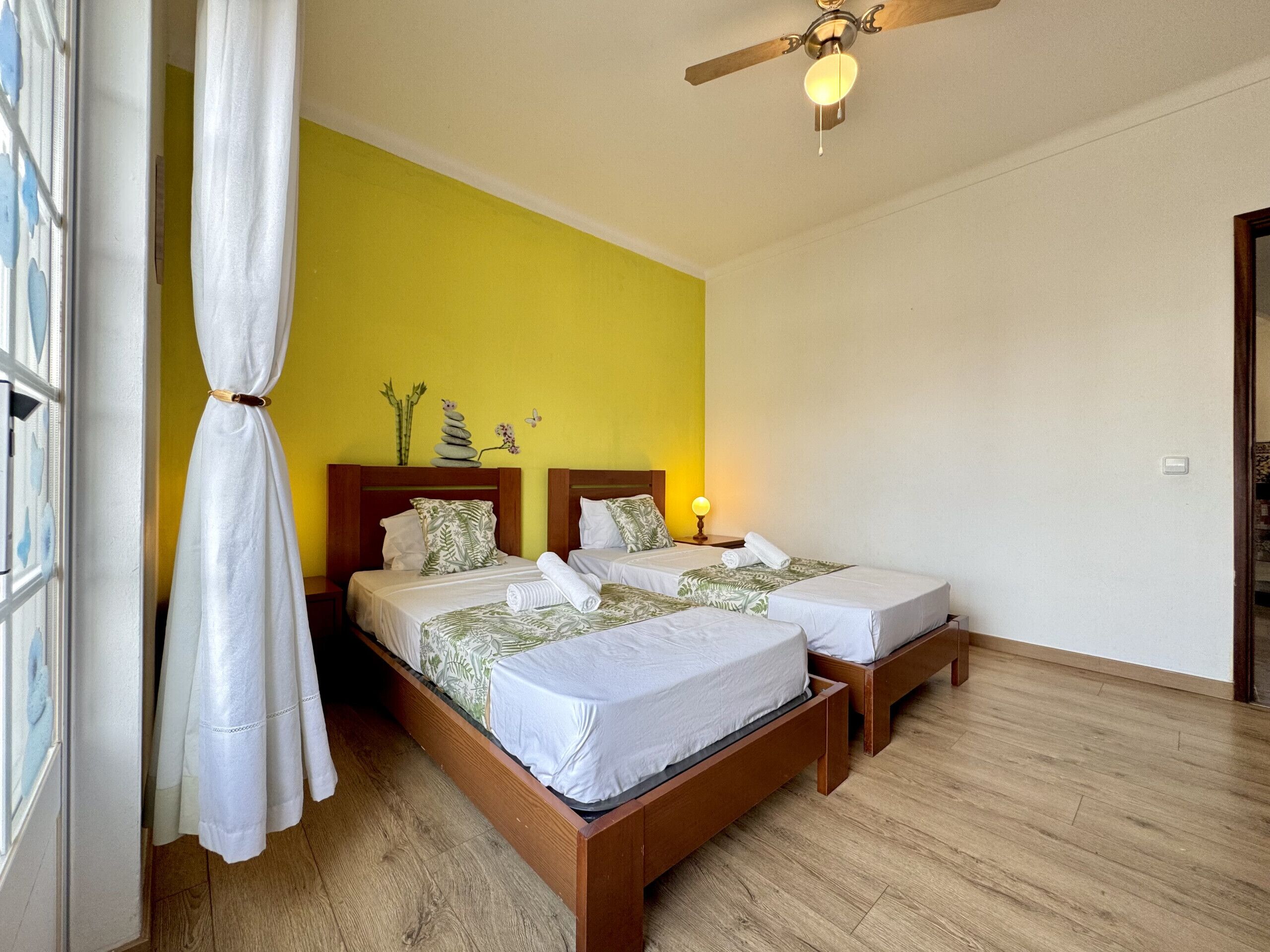 A hotel room with two beds, a ceiling fan, and a window with curtains.