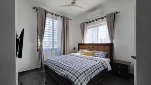 A bedroom with a bed, a nightstand, a ceiling fan, and a window with curtains. - Cozy 2-bedroom + 1 hall house in charming Madina Estate in Accra with AC. (Madina)